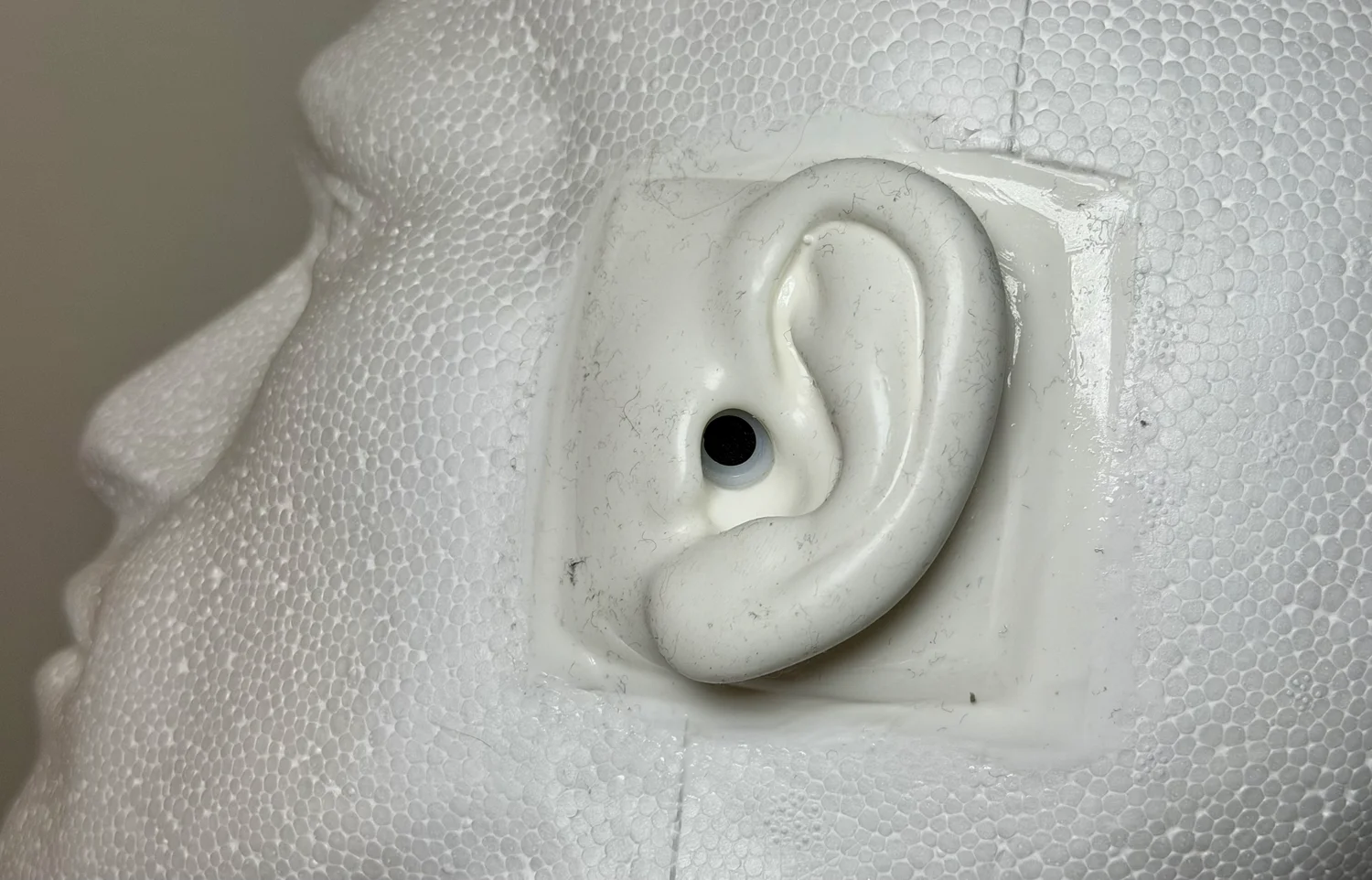 Close-up of the SR3D dummy head's silicone ear with the HD 650 earcup lifted away, showing the Primo EM272 electret capsule seated at the ear canal entrance