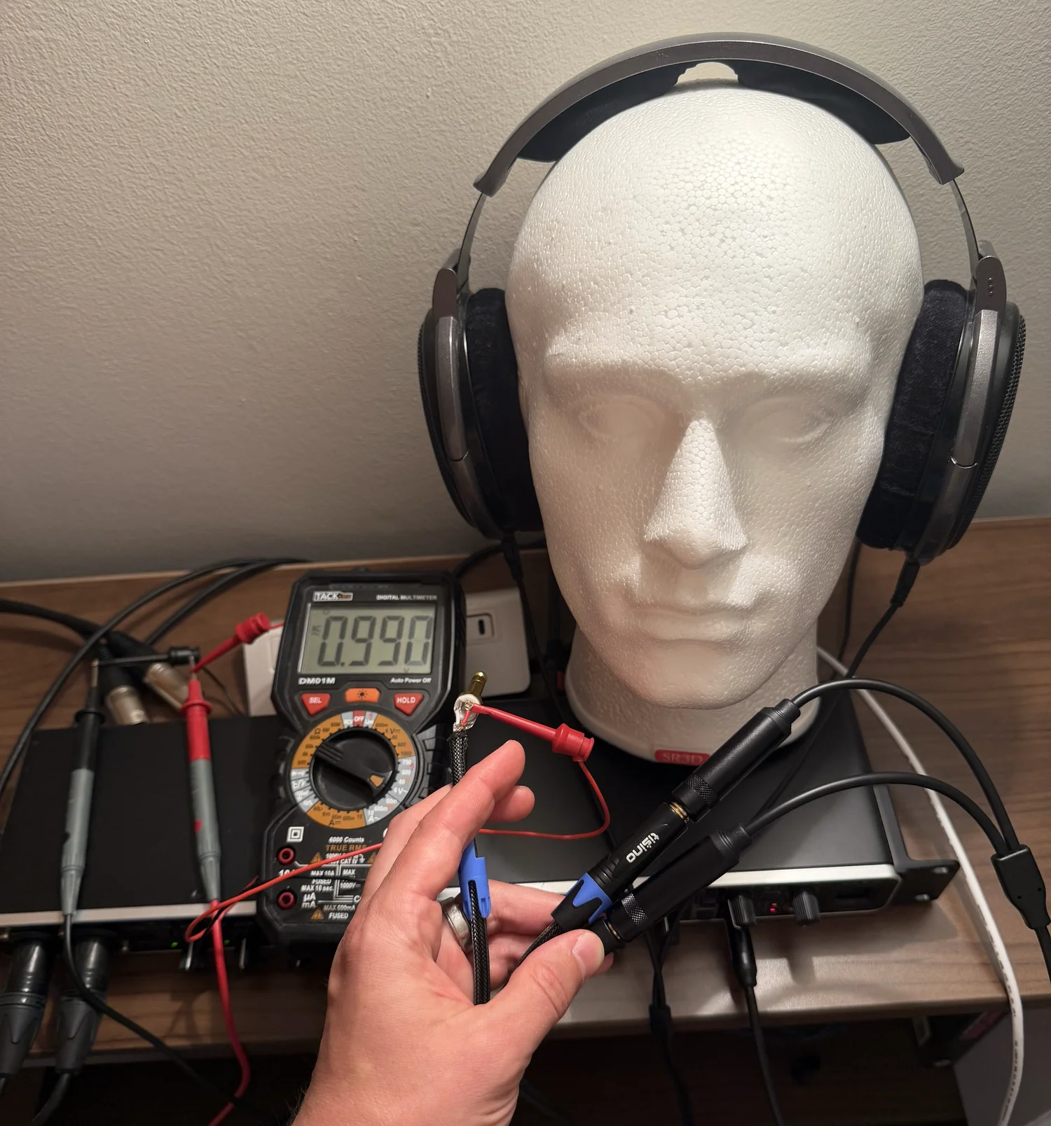 True-RMS multimeter probes on the quarter-inch Y-splitter measuring AC voltage across the HD 650 terminals while a 1 kHz calibration tone plays, headphones still connected and on the dummy head